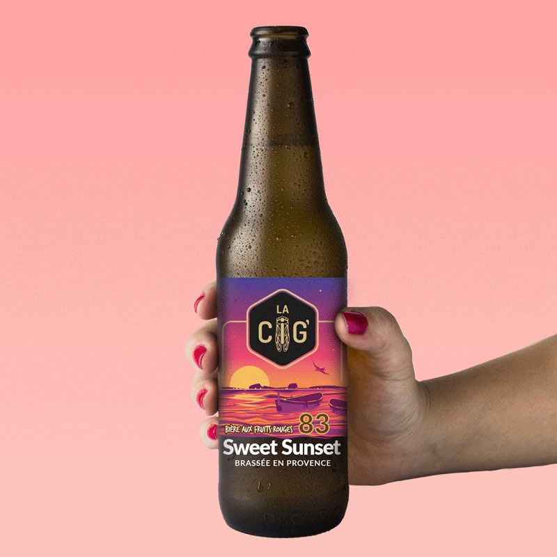 Main soutenant une bouteille de bière Sweet Sunset aux fruits rouges, avec étiquette transparente et colorée pour la brasserie La Cig, située à la Seyne-sur-Mer dans le Var, crées par Yunaima Oyola, Yo Design.