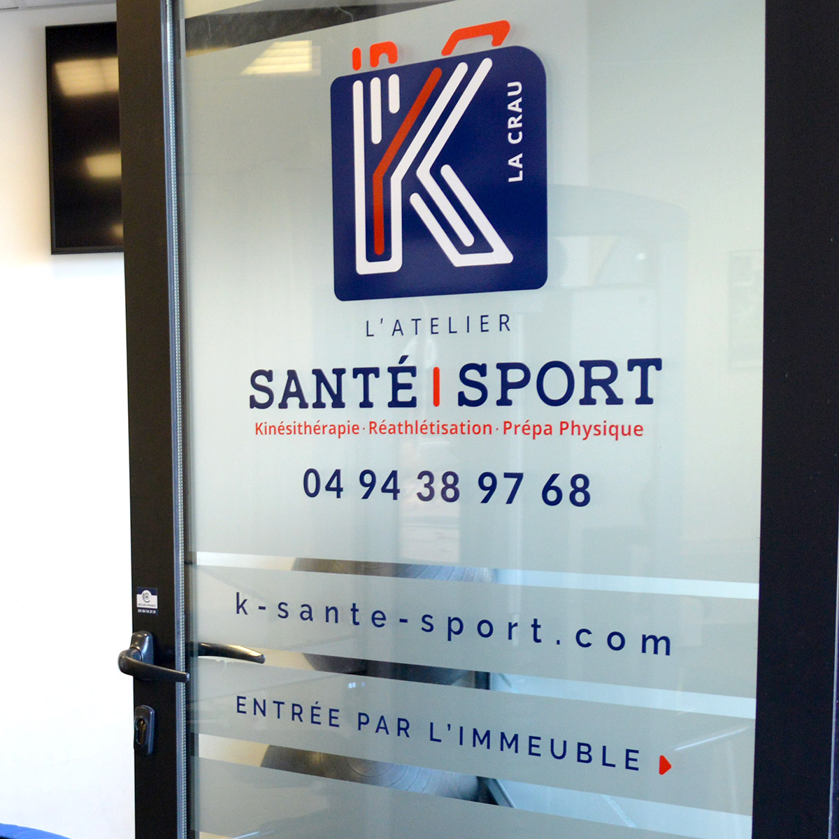 Flocage vitrine et porte contenant le logo bleu et orange aux formes arrondies et modernes pour K Santé Sport, cabinet de kinésithérapie situé à La Crau dans le Var, créé par Yunaima Oyola, Yo Design, graphiste et web-designer basée à Cherbourg-en-Cotentin