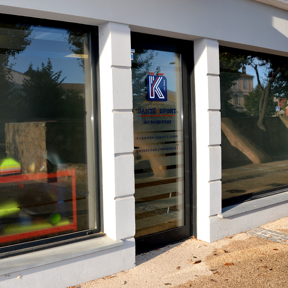 Flocage vitrine contenant le logo bleu et orange aux formes arrondies et modernes pour K Santé Sport, cabinet de kinésithérapie situé à La Crau dans le Var, créé par Yunaima Oyola, Yo Design, graphiste et web-designer basée à Cherbourg-en-Cotentin